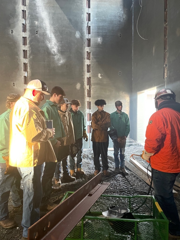 Students watching someone get ready to weld.